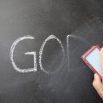 Tulisan GOD pada papan tulis hitam yang sedang dihapus sebagai ilustrasi ketidakpercayaan terhadap Tuhan