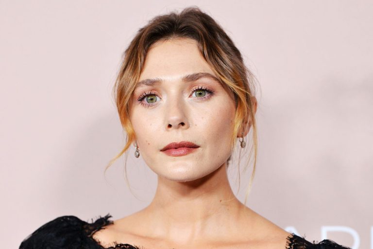 Elizabeth Olsen tersenyum dengan rambut pirang bergelombang, mengenakan gaun hitam elegan